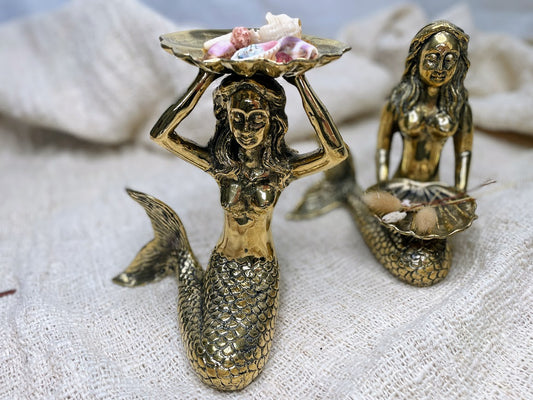 Two brass mermaid statues decorated with a coastal aesthetic and shells