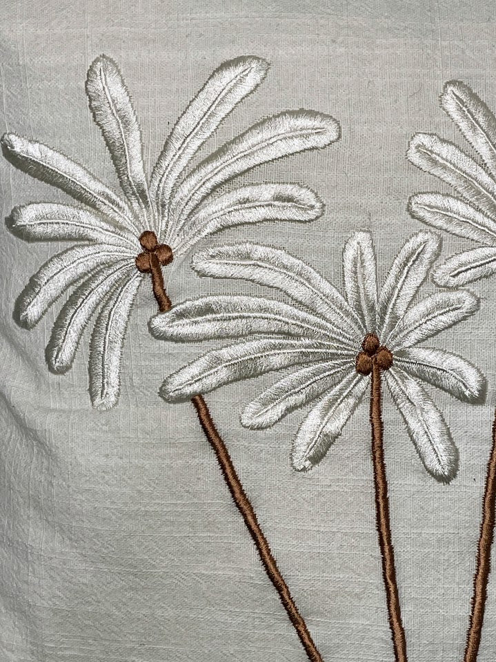 Close up details of white leaves and brown coconuts and stalks hand sewn palm trees on linen cushion
