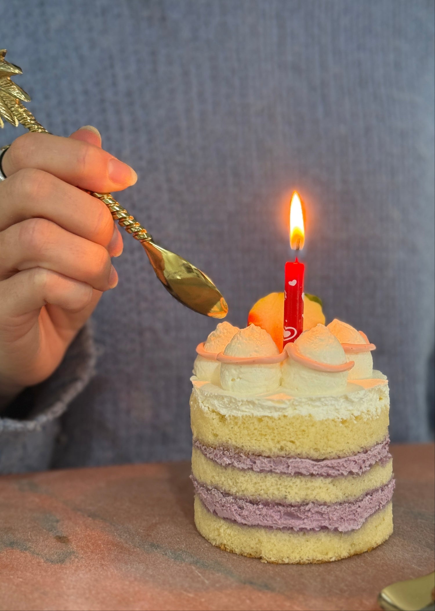 Small layered cake with a lit candle and a hand holding a spoon near it.