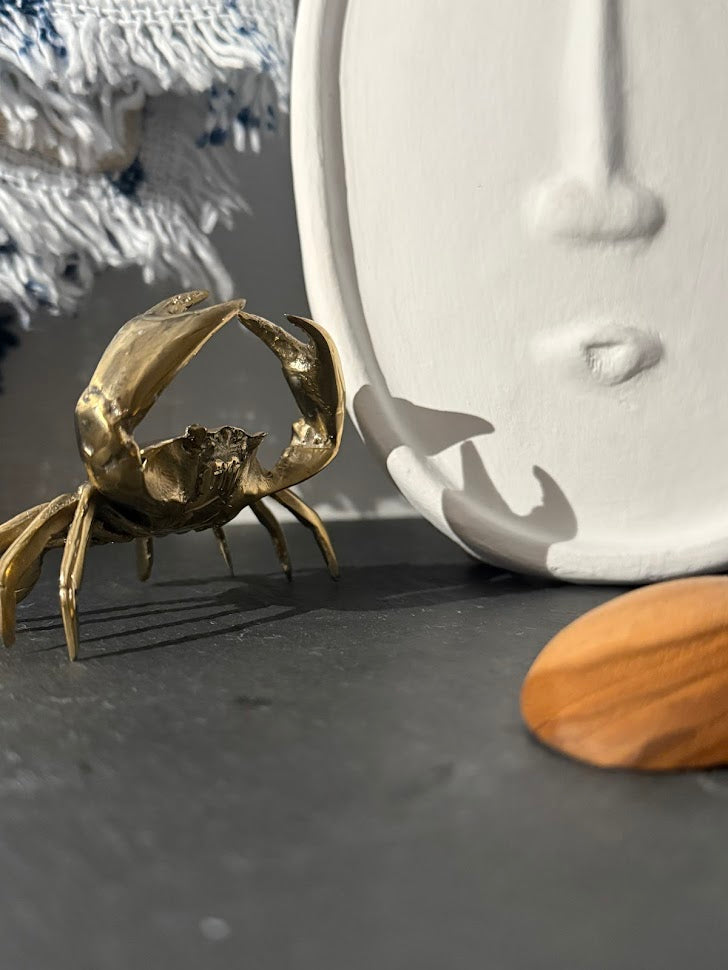 Gold crab figurine next to a white ceramic faece decor on a dark surface.