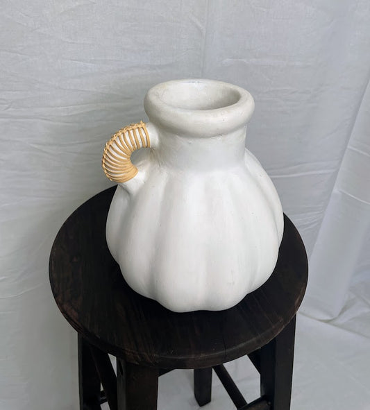White terracotta vase with single rattan wrapped handle, sitting on a wooden stool