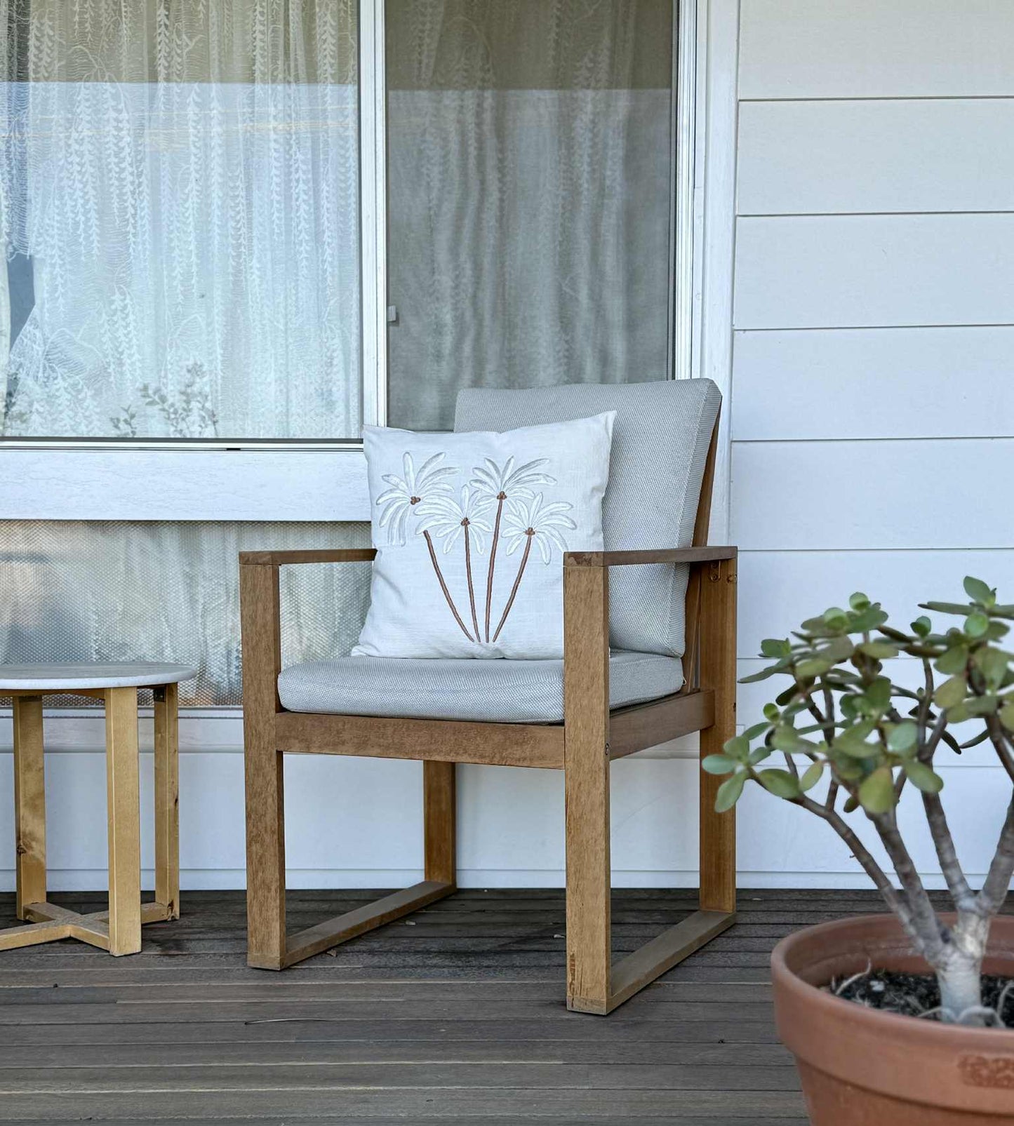 Outdoor furniture with a cushioned chair and table on a wooden deck, featuring a potted plant.