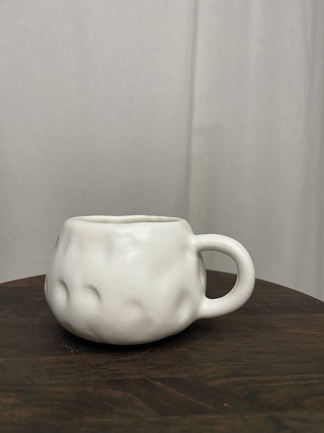 All white back of a short and round mug with hand crafted dimples