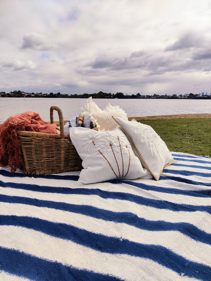 Picnic setting with basket, throw rugs and cushions by a river