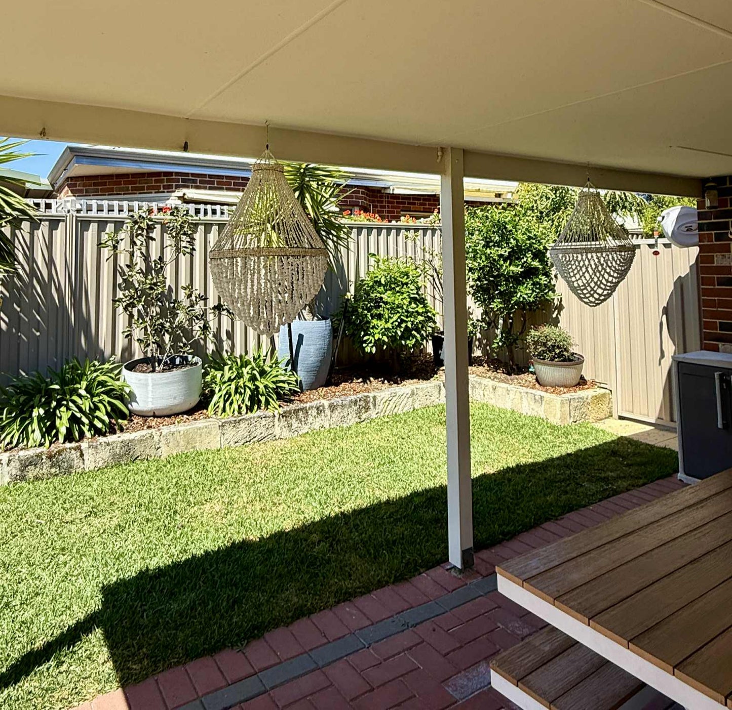 Covered patio area with plants and a garden view, showcasing two shell pendants