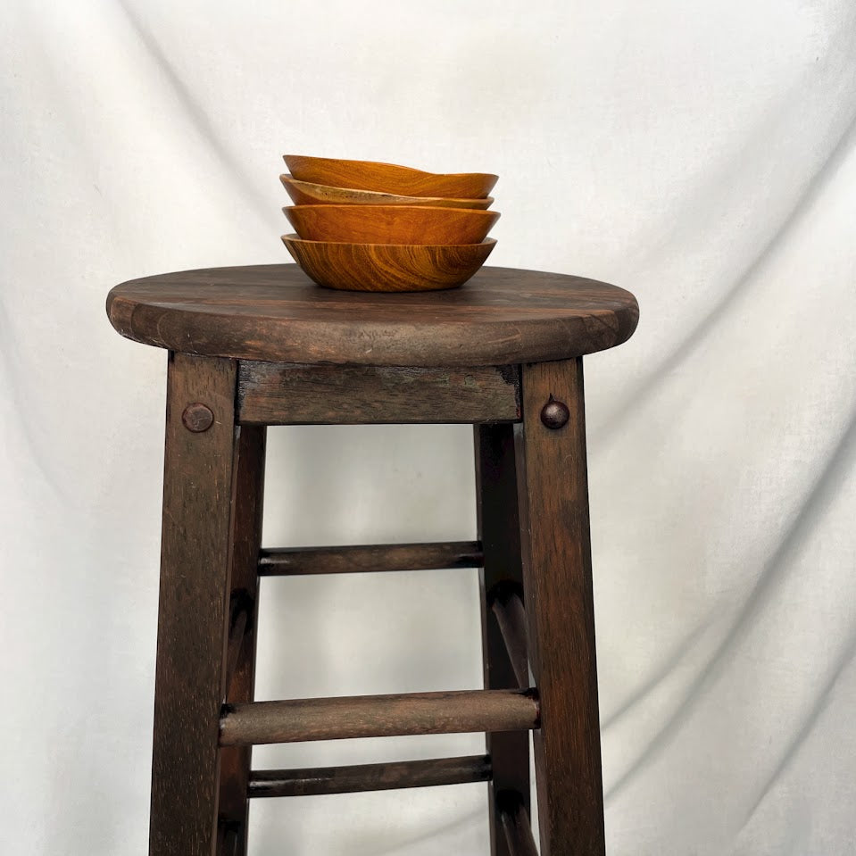 A stack of teak root wooden bowls on top of a wooden stool, shot in a studio setting