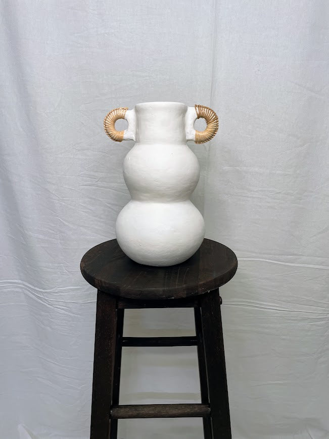 Tall white pottery vase pot with two small rattan wrapped handle on the top of the pot, in a studio setting