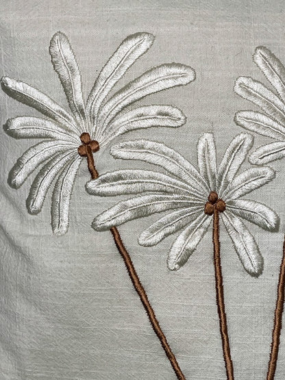 Close up details of white leaves and brown coconuts and stalks hand sewn palm trees on linen cushion