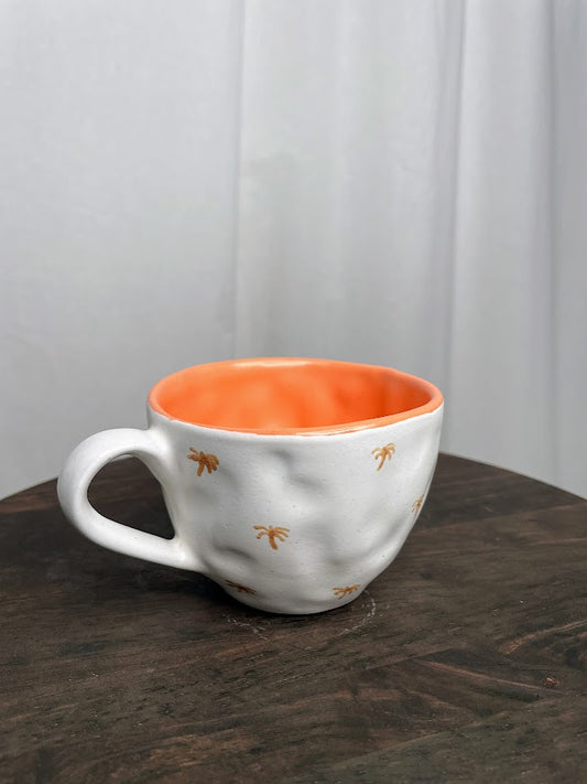 White mug with burnt orange mini palm trees painted on the outside, and a solid orange inside
