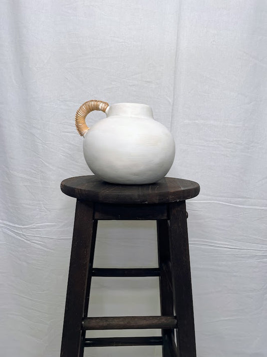Short round white pottery vase pot with single rattan wrapped handle placed on a wooden stool