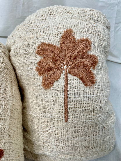 Close up details of brown terracotta hand embroidered palm tree, sewn onto natural linen throw blanket