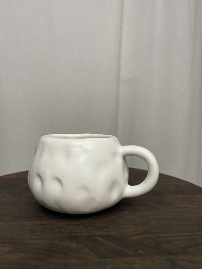 All white back of a short and round mug with hand crafted dimples