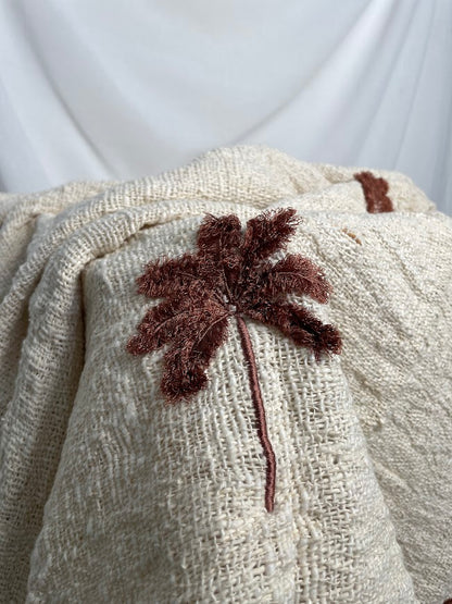 Close up details of wine coloured hand embroidered palm tree on linen throw rug
