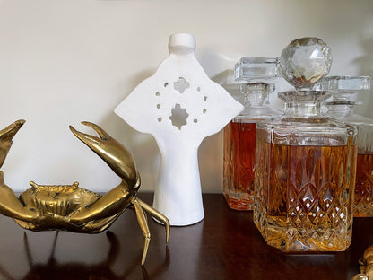 White candle holder on a bar with decanters and brass crab