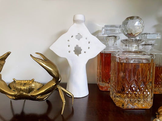 White candle holder on a bar with decanters and brass crab