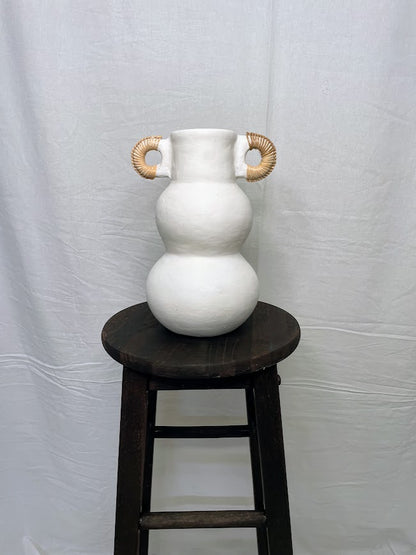 Tall white pottery vase pot with two small rattan wrapped handle on the top of the pot, in a studio setting