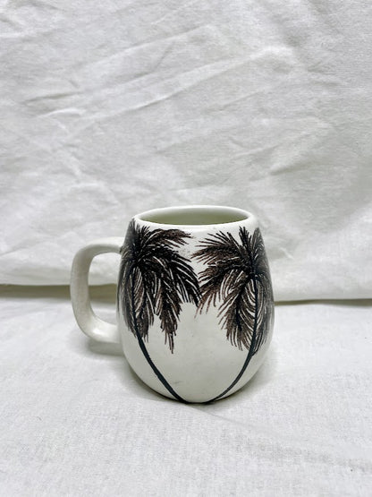 Tall white mug with black palm trees painted on one side
