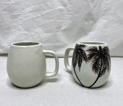 Front and back view of a tall white mug with front painted with black palm tree