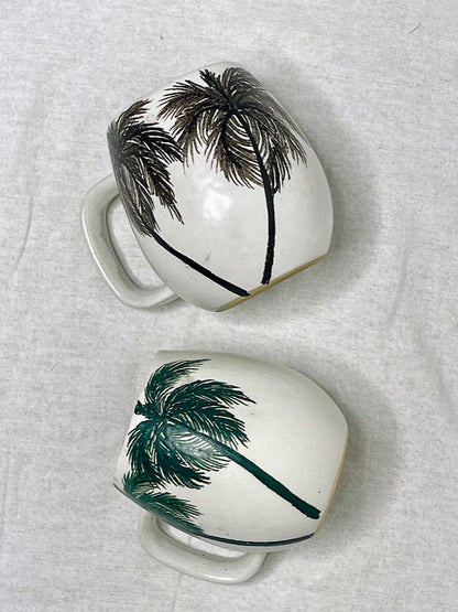Flay lay of two tall hand crafted mugs, with detailed hand painted palm trees